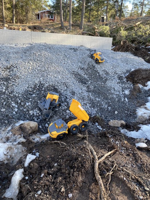 Lekfordon på grushög vid en byggarbetsplats med skogsbakgrund och snörester.