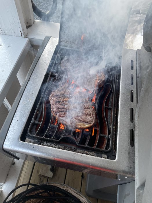 Kött grillas på en gasolgrill, rökigt, utomhus på däck, grillränder synliga.