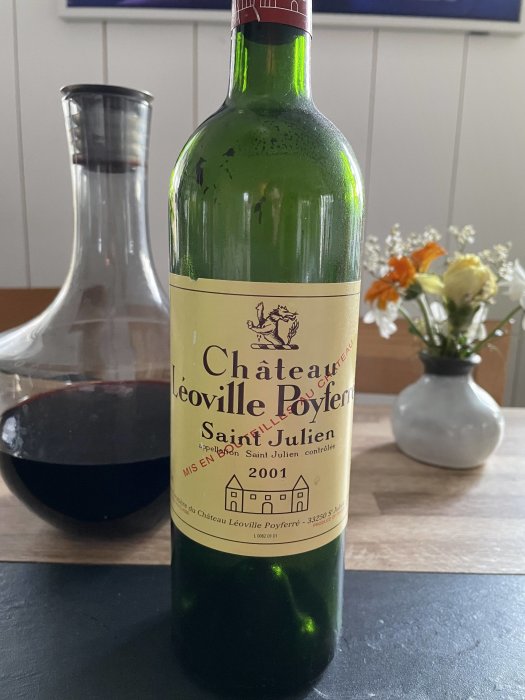 Flaska vin, etikett Château Léoville Poyferré 2001, karaff, rödvin, blommor i bakgrunden, inomhus.