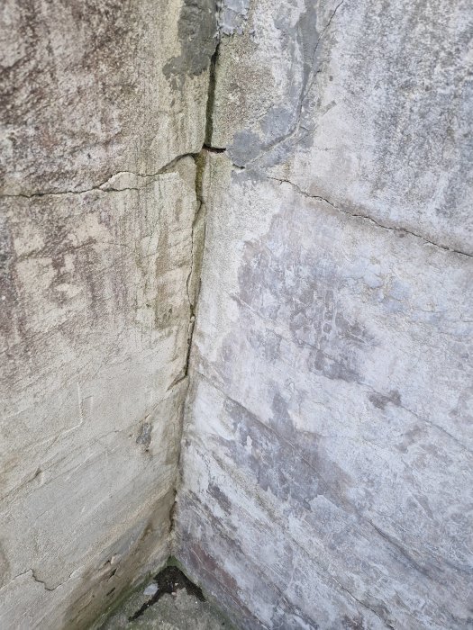 Slitet hörn av en betongvägg med sprickor och missfärgningar.