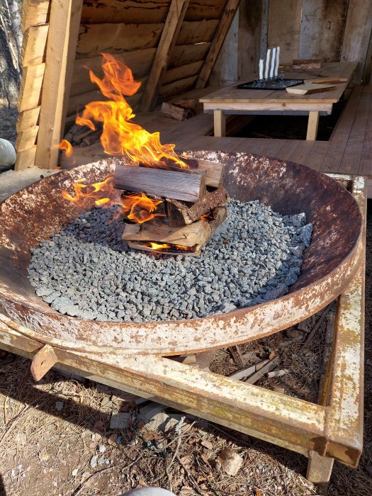 Eld i rostig behållare, stenkol, utomhus träbord med ljusstakar, traditionell smidesmiljö.