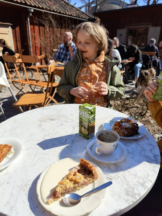 Utomhusfika: kaffe, paj, bulle, person, soligt cafébord.