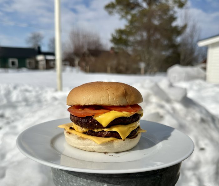 Dubbel cheeseburgare på tallrik utomhus med snöig bakgrund och soligt väder.