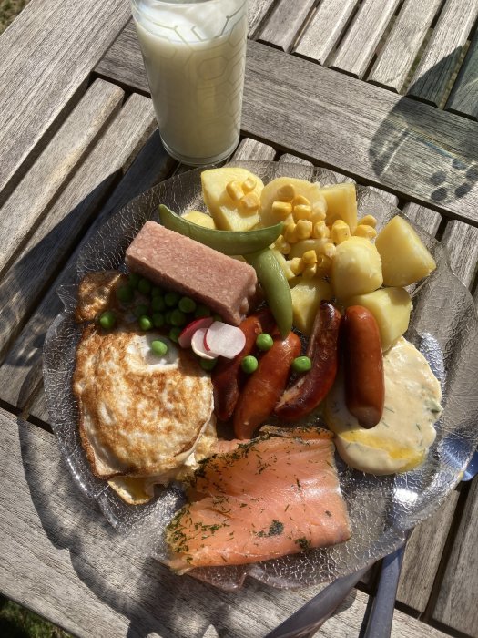 En tallrik med blandad mat och ett glas mjölk på ett träbord utomhus.