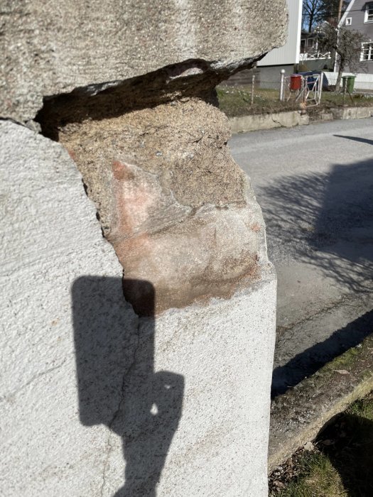 Erosion eller skada på betongstruktur med exponerad armering och skugga av en person som fotograferar.