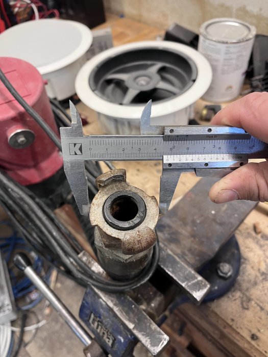 Mätkäke mäter en metallkomponents diameter i en verkstadsmiljö. Verktyg och maskiner i bakgrunden.