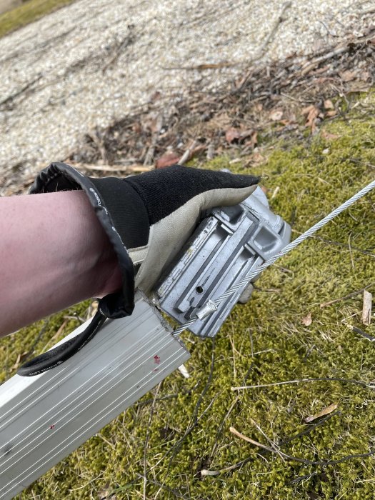 En person håller en avskuren aluminiumprofil och genomsiktlig slang med handske på en gräsmatta.