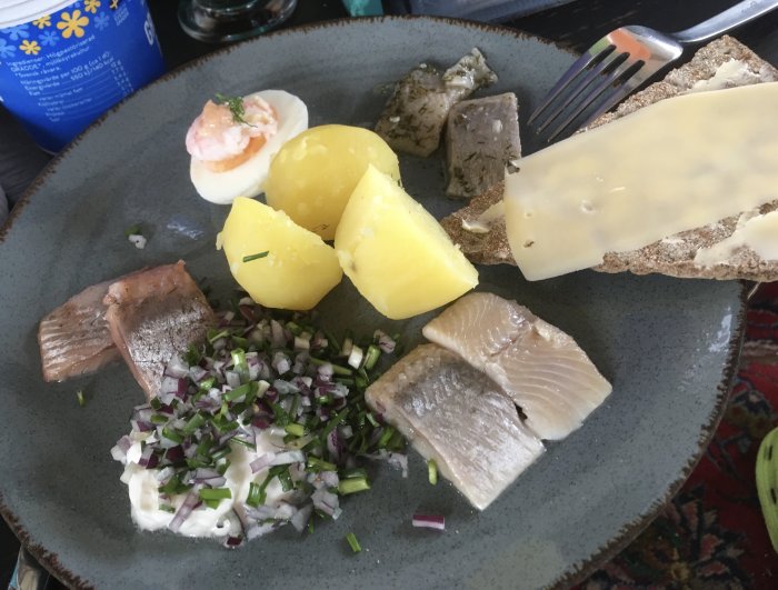 Traditionell svensk måltid med sill, potatis, knäckebröd med ost, ägg och gräddfil med gräslök.