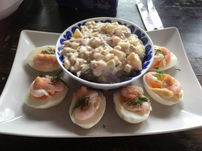 Ett fat med halverade ägg toppade med räkor och dill, serveras med skaldjursallad.