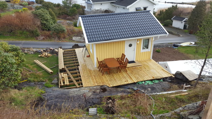 Ett gult hus med en ny byggd träveranda och oorganiserat byggmaterial på marken.