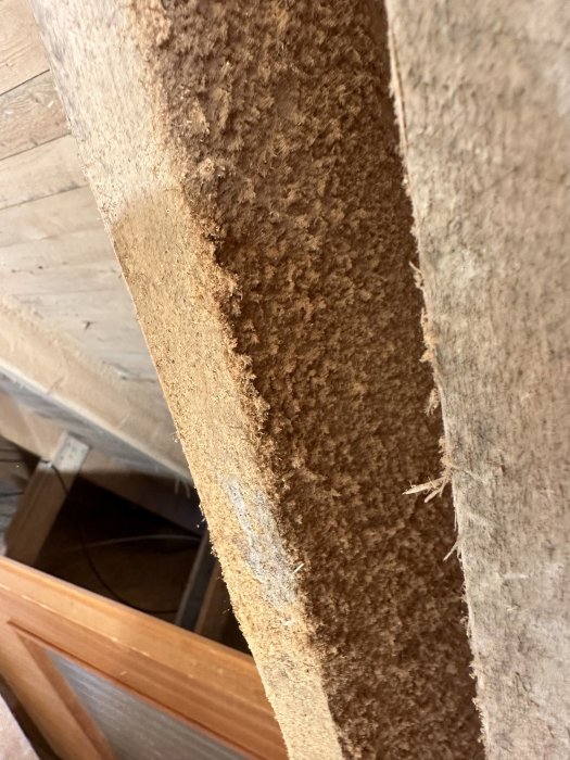 Närbild på träbjälke med isoleringsmaterial, textur och trädetalj synlig, potentiellt en byggnadskonstruktion.