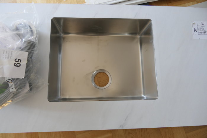 En rostfri diskbänk ligger på ett bord. Förpackningar och papper syns i bakgrunden.