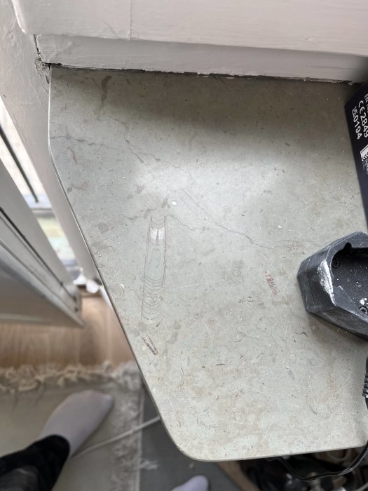 Närbild av skadad vit dörrkarm ovanför smutsigt stengolv med skor och en svart föremål nedanför.
