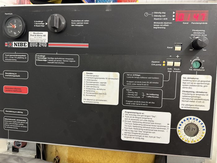 Värmepumpspanel med instruktioner, vred, knappar, mätare och digital klocka. Märkt NIBE och Stockholm Pool & Värme AB.