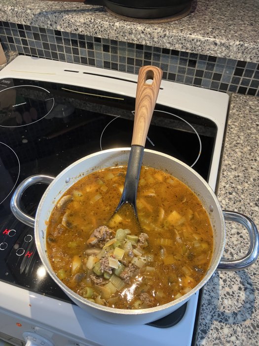 En stor gryta med kött och grönsakssoppa på spis, träredskap, modern kök miljö.