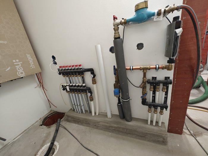 Ett oavslutat VVS-installationsprojekt med rör, kulventiler och en vattenfördelare på en vägg.