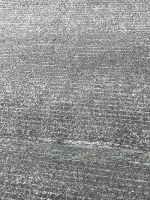 Grå betongyta med texturmönster, sprickor och linjer. Slitstarkt, robust material. Vertikal orientering.