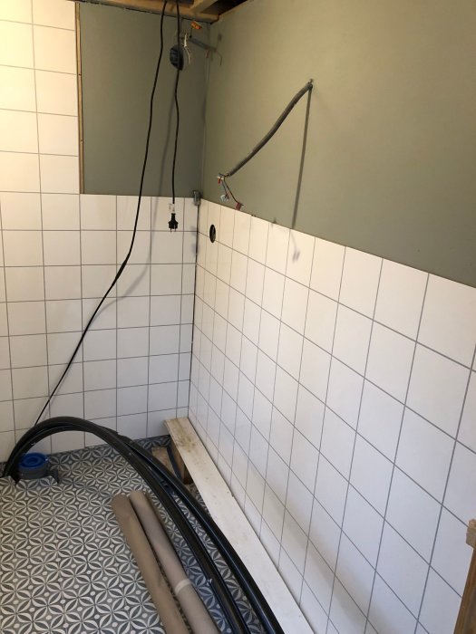 Renovering av badrum, kaklade väggar, öppet tak, rör och kablar synliga, byggmaterial på golvet.