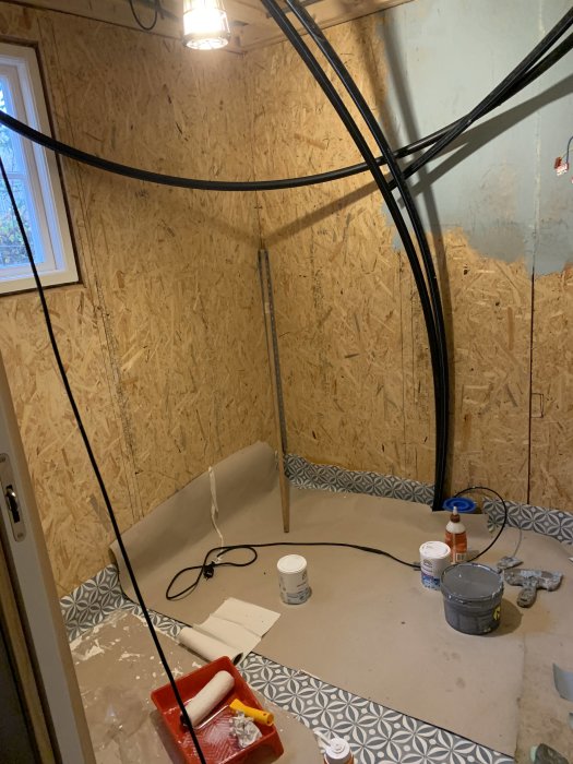 Under renovering, osäkerad OSB-väggar, kablar, målarverktyg, golv under arbete, oavslutat badrumsprojekt.