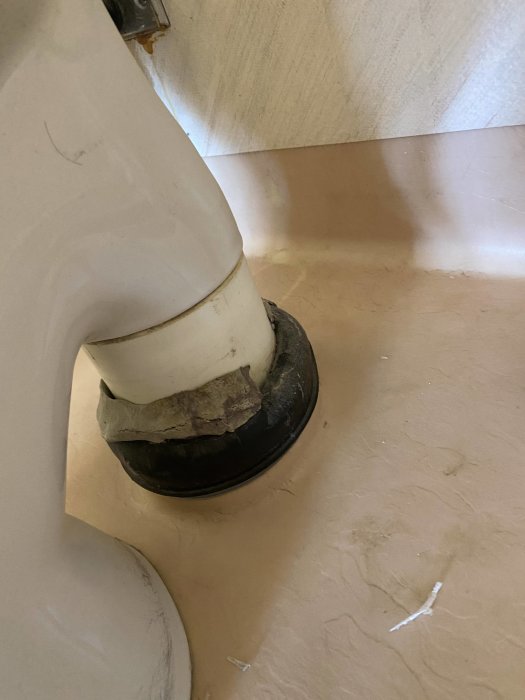 Vit röranslutning till ett handfat med synlig smuts och slitage.