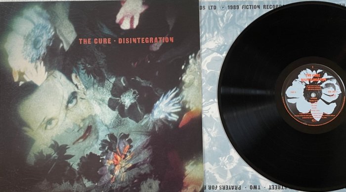 Vinylskiva och omslag för albumet "Disintegration" av The Cure, mörka toner, blommiga element, överlagrad porträttbild.