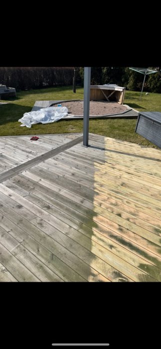 Trädäck i förgrunden, omkullvält rund pool och leksak i en trädgård, soligt väder.