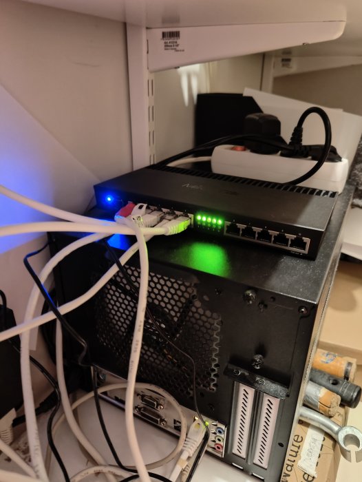 Nätverksutrustning med många kablar i en trång plats, inkluderar switch och annan elektronisk apparatur.