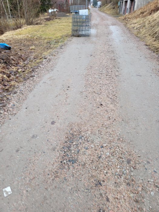 Grusväg, metallstaket, grå himmel, bar mark, inget snö, vinter- eller höstlandskap, utomhus, dagtid, ensamt landskap.