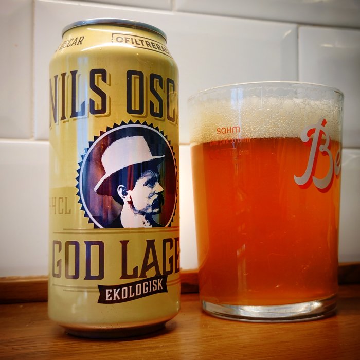 Ölburk med texten "NILS OSCAR GOD LAGER EKOLOGISK" bredvid ett glas med öl.