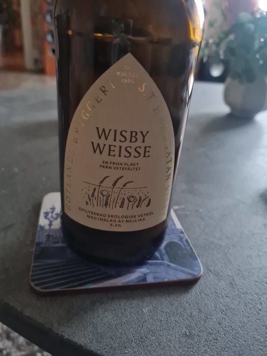 Ölflaska, "Wisby Weisse", etikett, ofiltrerad ekologisk veteöl, 5,2 % alkohol, på coaster. Inomhus, oskarp bakgrund.