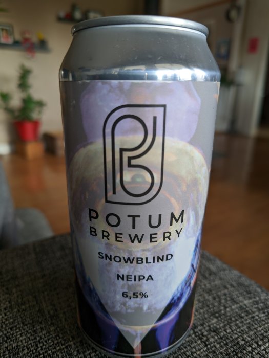 Aluminiumburk med etikett "Potum Brewery Snowblind NEIPA", alkoholhalt 6,5%, hålls inomhus, suddig bakgrund.