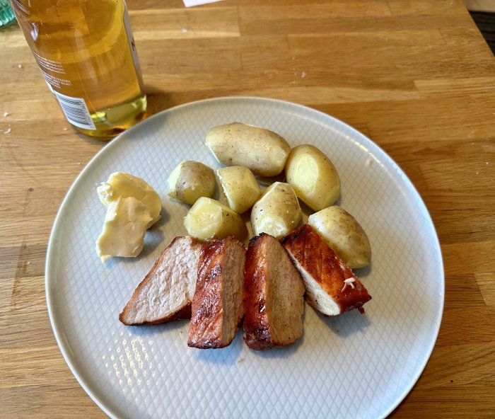 En tallrik med stekt kött, kokta potatisar och sås, bredvid en flaska olivolja.