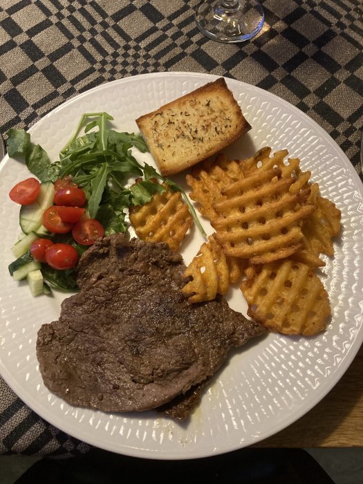 Stekt biff, våffel-pommes frites, vitlöksbröd och sallad på rutig duk.