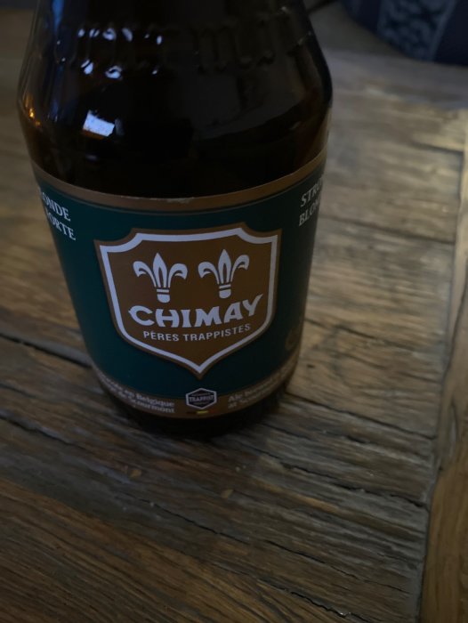 En ölflaska med märket Chimay på ett träbord. En del av etiketten är synlig.