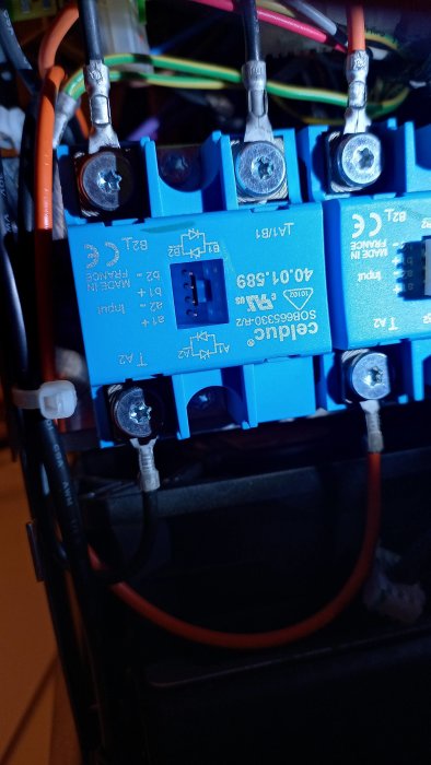 Blåa elektriska skruvplintar med kablar, märkningar, i dunkelt upplyst teknisk miljö.