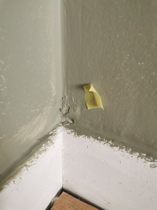 Skadad vägg och list med flagande färg och en bit tejp i ett hörn.