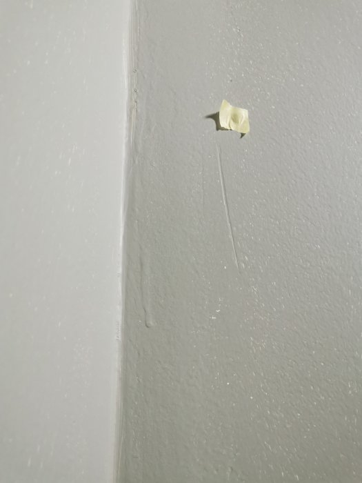 En bit maskeringstejp sitter på en grå vägg med spår av droppande vätska under. Enkel, oansenlig, vardaglig scen.