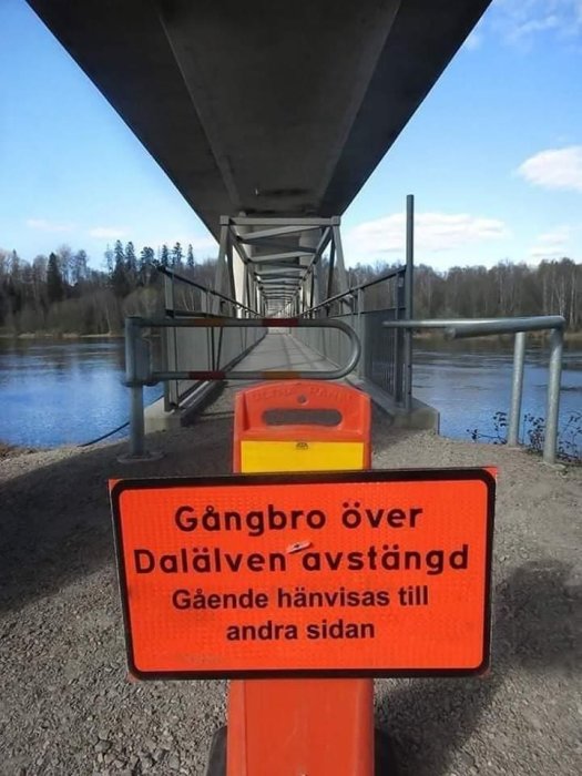 Skylt varnar att gångbro över Dalälven är avstängd, hänvisar till andra sidan, paradoxal situation.