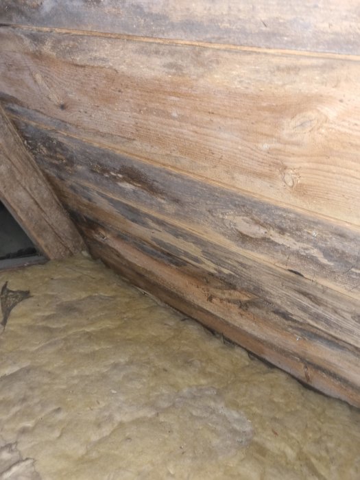Trävägg möter isoleringsmaterial, möjligen i ett byggnads- eller renoveringssammanhang. Strukturer och material möts i en vinkel.