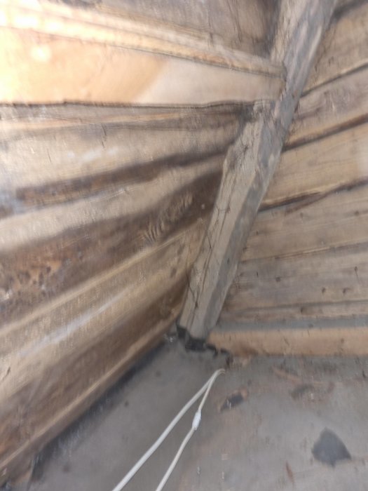 Suddig bild av ett hörn med träväggar och golv, kabel längs golvet.