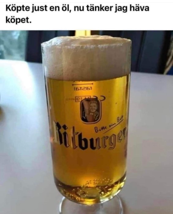 Ölglas överfullt med skum, Bitburger-märke, skämtsamt textmeddelande om att "häva köpet".