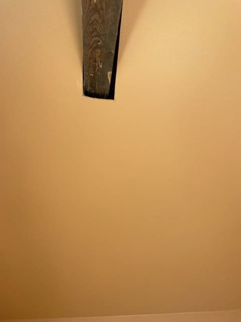 Ett trästycke sticker ut från en beige vägg, enkelt och abstrakt med dämpad belysning.