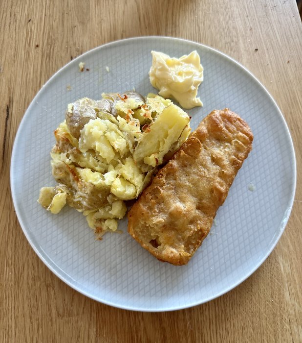 En tallrik med potatismos, smörklick, och en fryst friterad fiskfilé.