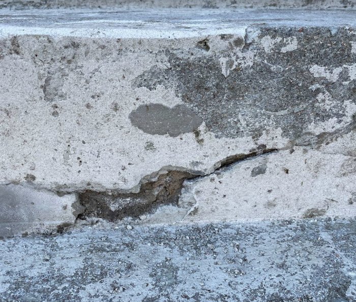 Närbild på skadad betongvägg med sprickor och erosion. Textur av förfall och nötning synlig.