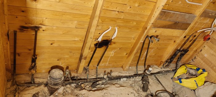 Rörgenomföring och elektriska ledningar i oavslutat väggutrymme, tecken på renovering eller byggkonstruktion, trä och murbruk.