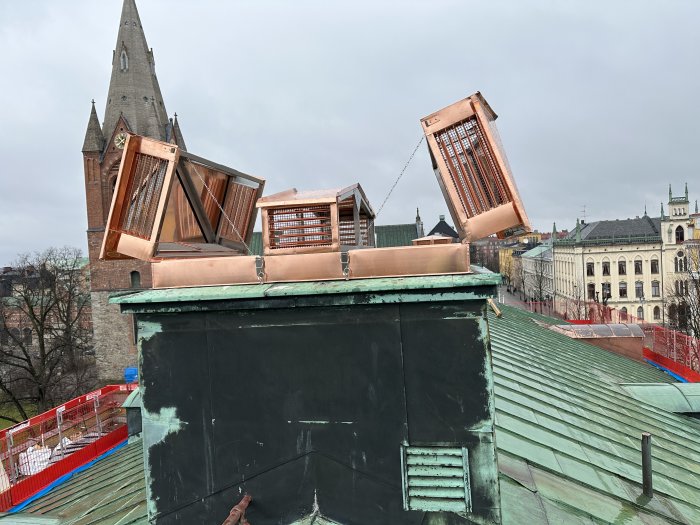 Utomhusventilation på tak med uppslagen kopparluckor, historisk kyrka i bakgrunden, molnig himmel.