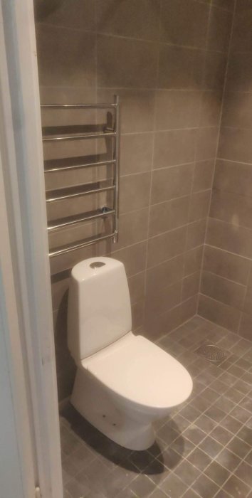 Modernt badrum med toalettstol, värmehanddukstork och kaklade väggar.