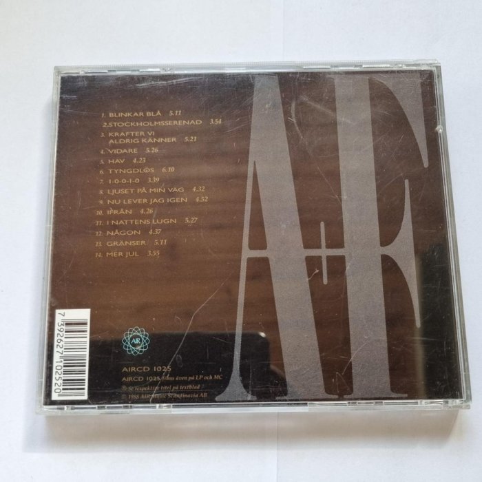 Ett CD-fodral med spårlista och delvis synligt grafiskt motiv, nött med repor och damm.