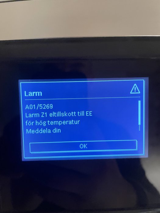 Digital skärm visar larmmeddelande om hög temperatur och instruktion att meddela någon.