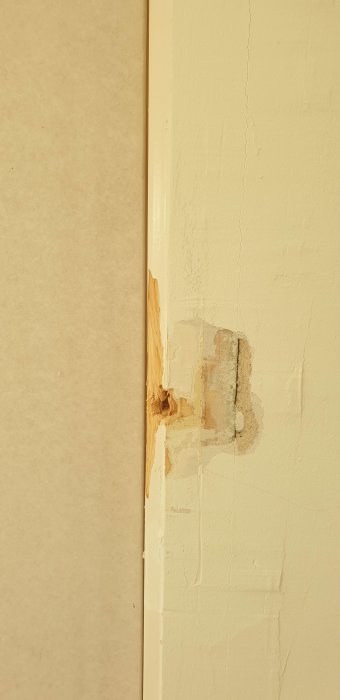 En skadad hörnkant med avskalad färg och spår av trä samt en sprucken vägg.